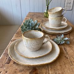 a wooden table topped with two cups and saucers filled with succulents