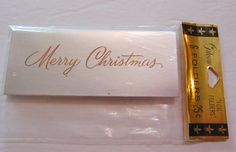 a white envelope with a gold pen and merry christmas message on the front, sitting next to it's packaging