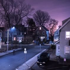 an empty street at night with some houses in the background and one car parked on the side