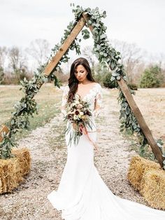 a woman in a wedding dress standing next to hay bales and holding a bouquet