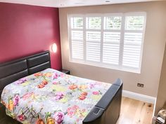 a bed sitting in a bedroom next to a window with shutters on the windowsill