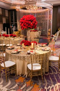 a table set up with red flowers and candles for a formal function in a ballroom