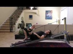 two people doing exercises on exercise equipment in a living room with stairs leading up to the second floor