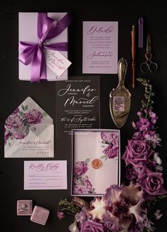 the wedding stationery is laid out with purple flowers and calligraphy on black paper