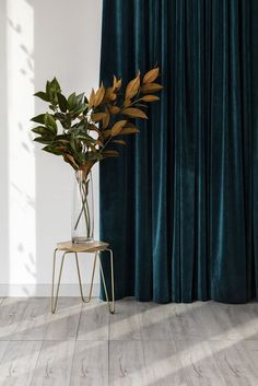 a plant in a vase sitting on a stool next to a curtain