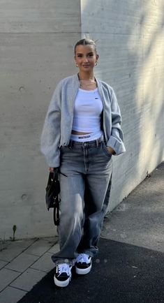 a woman standing in front of a white wall wearing grey jeans and a crop top