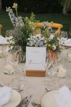 the table is set with place cards, wine glasses, and flowers in vases