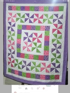 a purple and green quilt hanging on a wall