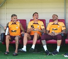 three men sitting on a bench laughing and looking at their cell phones in front of them