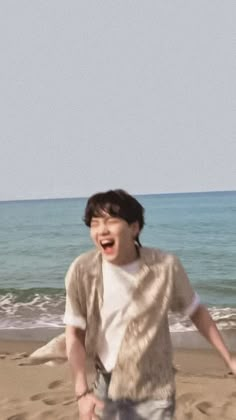 a young man standing on top of a sandy beach next to the ocean with his mouth open