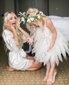 two women in white dresses and flowers on their heads, one is kneeling down while the other