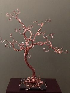 a wire tree sculpture sitting on top of a wooden table next to a gray wall