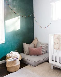 a baby's room with a crib, chair, and wall painted in teal