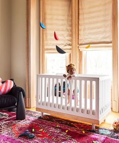 a baby's room with a crib, chair and window covered in blinds