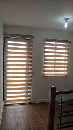 an empty room with two windows and wooden blinds