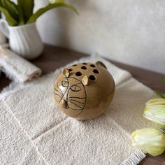 a ceramic cat sitting on top of a white rug next to some tulips