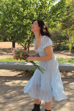 a woman in a blue dress holding flowers and looking up at the sky with her eyes closed