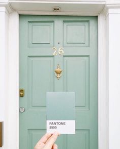 a person holding up a pantone paint color in front of a door with the number 26 on it