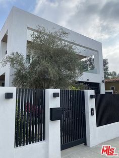 a white house with a black gate and trees in front of it on a cloudy day