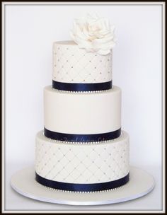 a three tiered white and blue wedding cake with a flower on the top layer