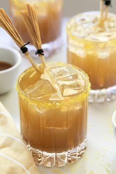 two glasses filled with drinks sitting on top of a white table next to bowls and spoons