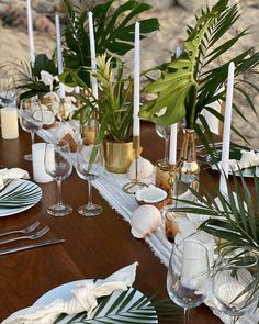 a long table with candles, plates and plants on it is set for a formal dinner