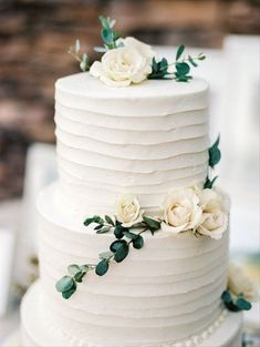 a white wedding cake with flowers and greenery on the top is sitting on a table