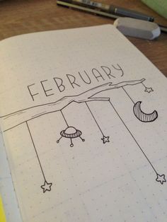 an open notebook with the words february written on it and drawings hanging from strings above them