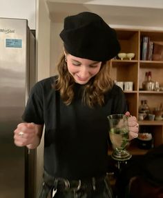 a woman holding a glass in front of a refrigerator