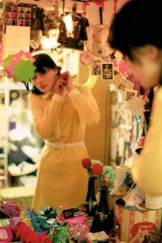 a woman standing in front of a mirror holding a cell phone to her ear and wearing a yellow dress