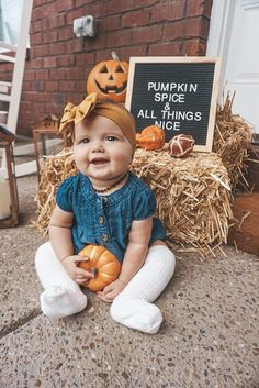 a baby sitting on the ground with pumpkins