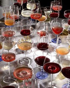 many glasses of wine are lined up on a silver tablecloth with white and red wines in them