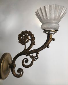 a wall light with a glass shade hanging from it's arm and an ornate design