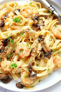 pasta with shrimp, mushrooms and parsley in a white bowl on a marble table