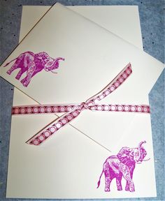 two envelopes with pink elephants on them and ribbon tied around the top, sitting next to each other