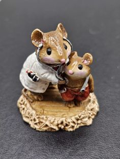 a figurine of two mice dressed in white and red clothes sitting on top of a piece of wood