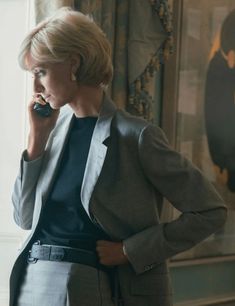 a woman standing in front of a window talking on a cell phone while wearing a suit