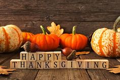 the words happy thanksgiving are spelled by scrabble blocks and acorns on a wooden surface