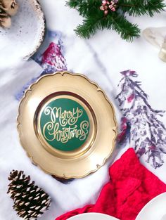 a plate with merry christmas written on it next to pine cones and other holiday decorations