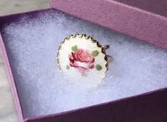 "This large vintage statement ring is decorated with a hand painted pink rose on white guilloche enamel. Set in gold tone metal, the white circle front has small swirl patterns in the enamel. The ring has a double band and fits comfortably on one's finger. Size: US Size 5 1/4. The ring is 1 1/8\" in diameter. This item weighs 9.2 oz. This item is in great vintage condition! There are no missing pieces or damages. Please feel free to contact us with any questions you may have about this item! **W White Enamel Ring For Gift, Rose Gold Enamel Ring, Vintage White Hand Painted Jewelry, Vintage Hand Painted White Jewelry, Round Flower Ring With Rose Design, Round Rose Design Flower Ring Gift, Round Flower Ring With Rose Design For Gift, Handmade White Enamel Ring Gift, Handmade White Enamel Ring For Gift