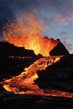 an orange and black lava is spewing out into the air at night time