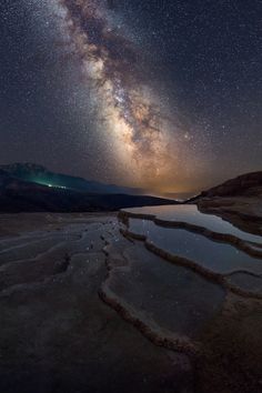 the night sky is filled with stars and milkys above a lake in an arid area