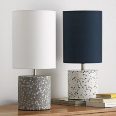 two lamps sitting on top of a wooden table next to books and a lamp shade