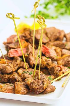 meat skewers on a white plate with lemons and parsley in the background