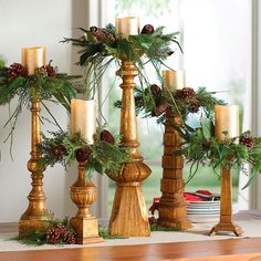 christmas decorations with pine cones and greenery in gold candlesticks on a mantle