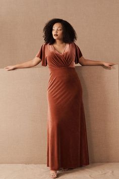 a woman standing in front of a wall wearing an orange dress and holding her arms out