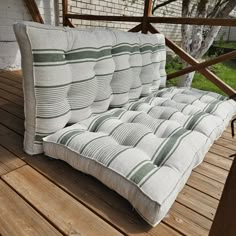 a white and green striped couch sitting on top of a wooden deck next to a tree