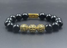 "This premium quality men's designer bracelet features 12mm polished black onyx beads accented with three handmade 12mm 22 karat gold plated sterling silver Bali beads and a 16mm x 8mm \"Bali Beads\" logo anchor bead. The gold is gently oxidized to darken the recessed areas. We use 1,2mm silicon stretch cord for superior strength. Your bracelet comes in a special presentation box. Choose your wrist size from the drop down menu. We will make your bracelet to fit. Check out our other Bracelets for Classic Black Bracelets With 8mm Beads, Black Wristband With 8mm Beads, Luxury Black Bracelets With 8mm Beads, Beads Logo, Gold Beads Bracelet, Mens Bracelet Designs, Mens Bracelet Black, Bracelet Luxury, Howlite Bracelet