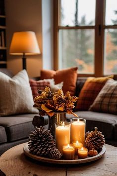 candles and pine cones sit on a tray in front of a couch