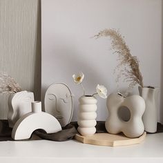 some white vases are sitting on a shelf next to flowers and other decorative items